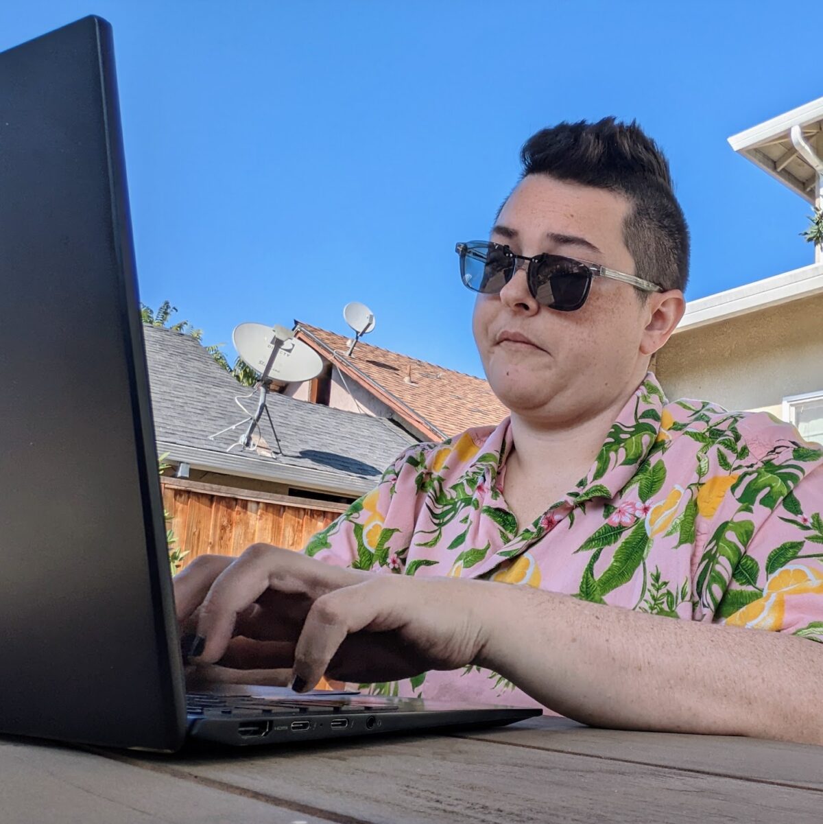 Selfie of a person typing on a laptop sitting outside